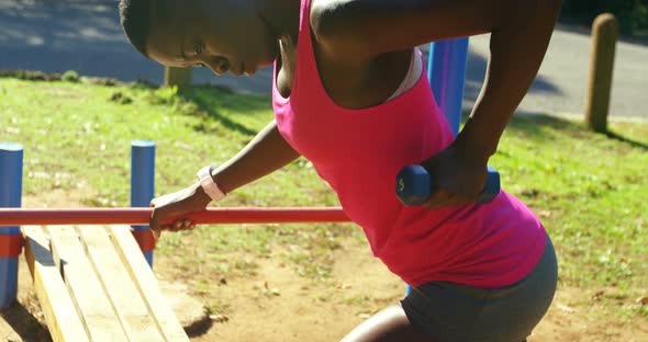 Female athlete exercising with dumbbell in the park
