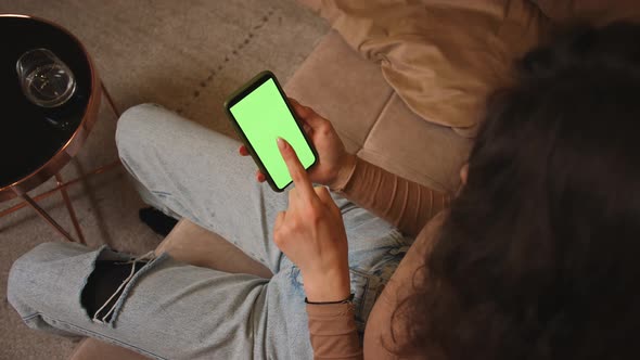 Closeup of Woman Holding Smartphone Chromakey Green Screen Watching Content Sitting on Couch at Home