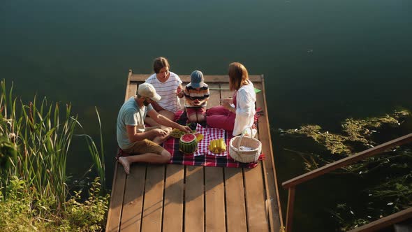 Friendly Family Enjoying Picnic on a Wooden Pier on Nature