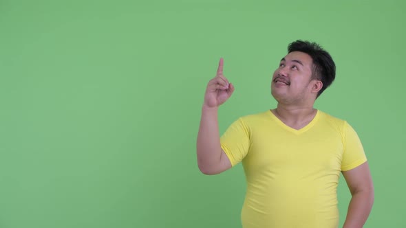 Happy Young Overweight Asian Man Talking While Pointing Up