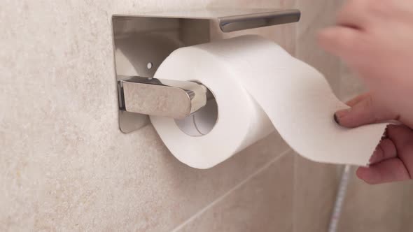 Men's Hands Unwind and Tear Off a Short Piece of Toilet Paper