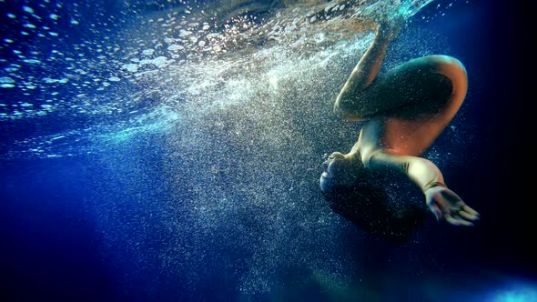 Woman is Floating Underwater Doing Somersault and Diving in Depth Dark Blue Water