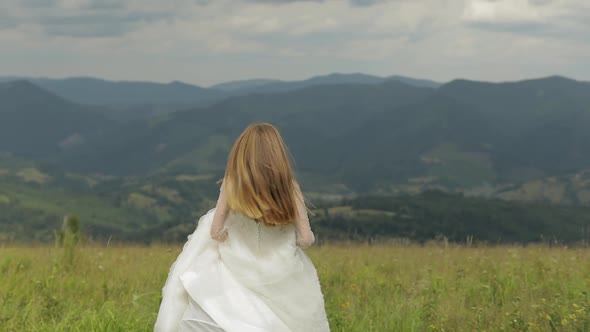 Beautiful Bride in Wedding Dress Running Through the Mountains Hills