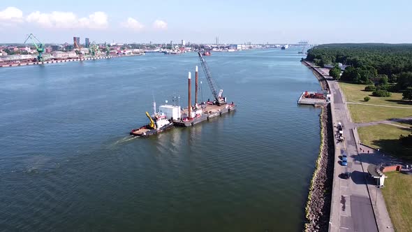 Tugboat pushing barge with crane on top to docks of Klaipeda harbor, aerial view