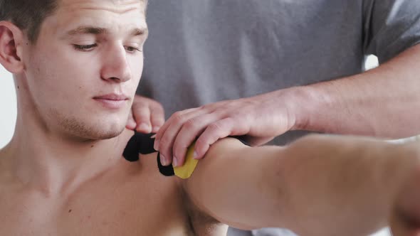 Physiotherapist Placing Kinesiology Tape on Shoulder of Athlete in Clinic