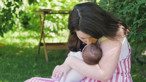 Mother with a Newborn Baby Walks in the Park. Young Mother Holds Her Baby in Her Arms. Breast