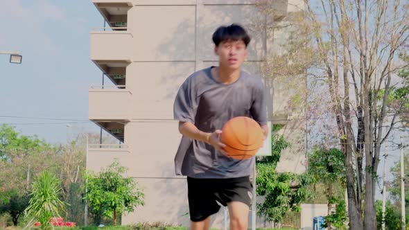 Young Asian athletic male playing basketball outdoors.