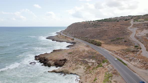 Epic drone shot of cars driving in cloudy mountain coastline background. Cinematic winding road