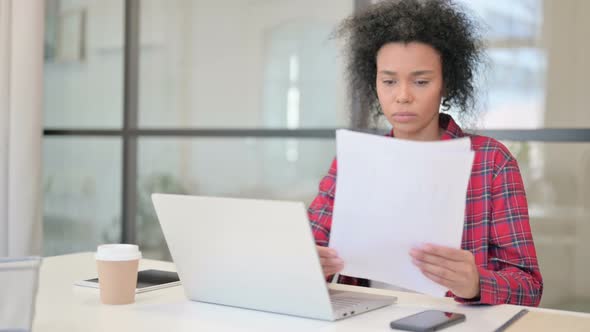 African Woman with Laptop Reading Documents in Office