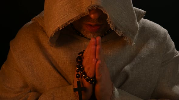 Monk in haircloth cowl robe praying in candlelight