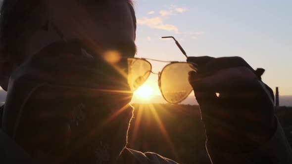 Close Up Unrecognizable Handsome Young Man in Black Bandana Against Sunset Background Puts on Black