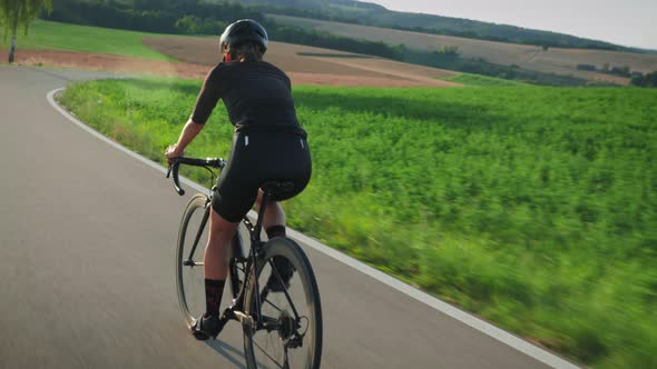 Road cycling. Female cyclist with fit and muscular body riding on bicycle at sunset