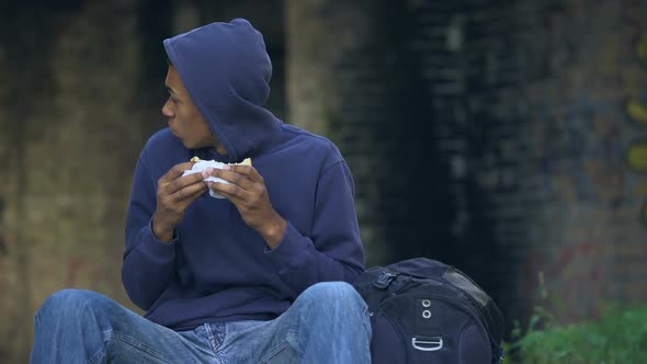 Starving Troubled Teen Chewing Snack Sitting Outdoors, Dangerous City Suburb