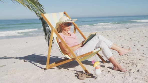 Senior Caucasian woman sitting on sunbeds at the beach.
