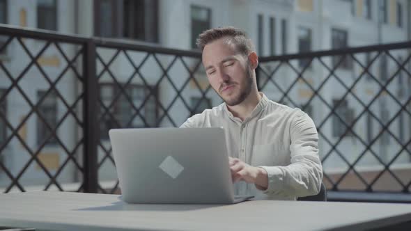 Portrait Confident Bearded Young Man Sitting at the Table on the Terrace in Front of Laptop, Working