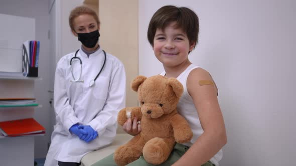 Portrait of Cheerful Caucasian Boy Posing with Teddy Bear in Coronavirus Vaccination Center