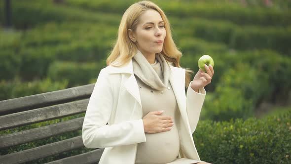 Happy Expecting Woman Biting Green Apple, Stroking Belly, Maternity Health Care