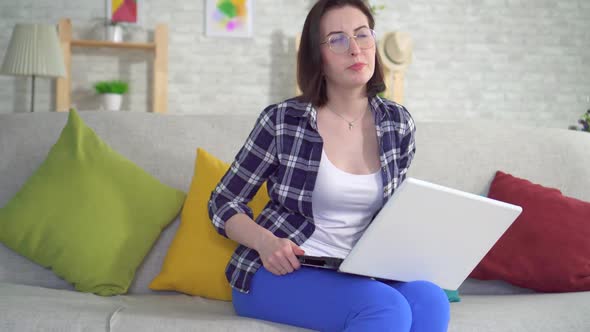 Woman Sitting on the Couch Working on a Laptop Is Experiencing Pain and Discomfort From Hemorrhoids