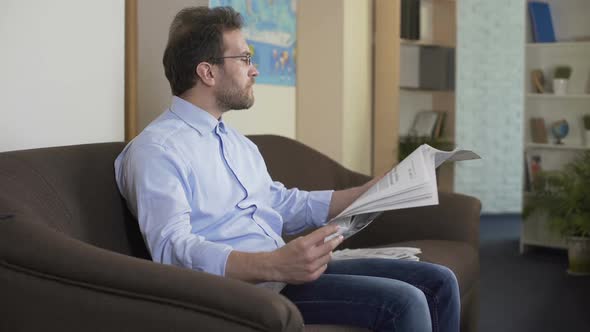 Morning Ritual, Relaxed Man Sitting on Couch and Reading Newspaper at Home