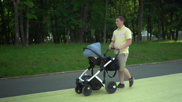 A Young Father Walks with a Pram in the Park Against the Backdrop of the Forest