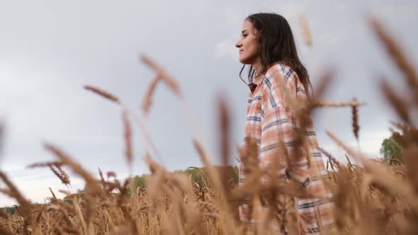 A Happy Girl in a Shirt Walks Across the Field and Touches Spikelets with Her Hands.