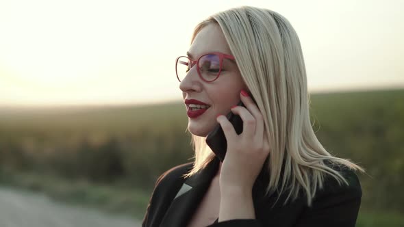 Happy Blonde with Red Lips in Glasses Talks on the Phone and Smiles at Terrace