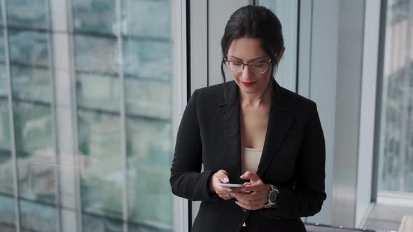 Portrait of a Young Woman in a Business Suit with a Mobile Phone in Her Hands