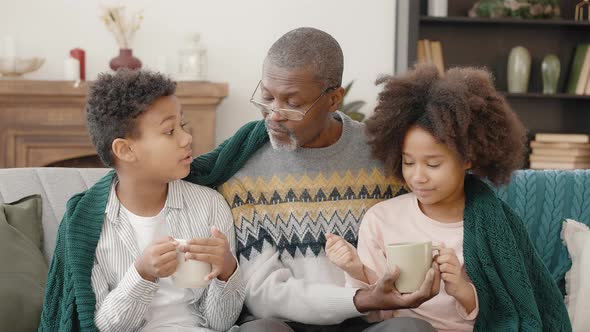 Positive African American Grandfather Sitting with Grandchildren Under Plaid Talking and Enjoying