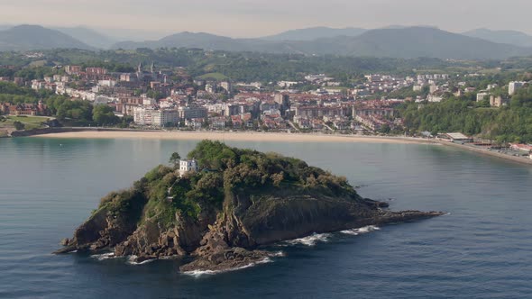 Lonely house in small rocky island with San Sebastian city in background, cinematic aerial view