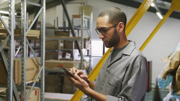 African American male car mechanic standing in a warehouse and using a tablet