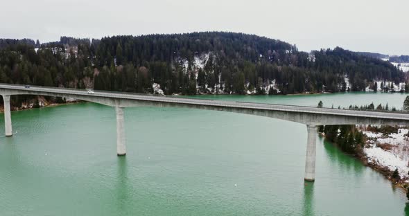 Quadcopter Video of a Bridge Across a River to Hills Covered in Snowy Forest