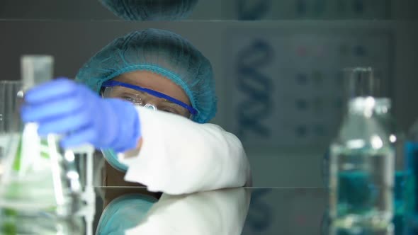 Lab Assistant Looking at Flask With Transparent Liquid Alcohol Production Spirit