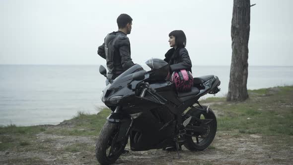 Wide Shot of Carefree Interracial Couple of Bikers Standing with Motorcycle on River Bank and