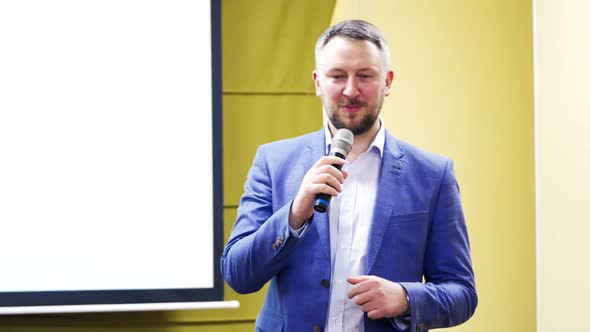 Professional coach in white shirt and blue suit speaking into the microphone in conference hall