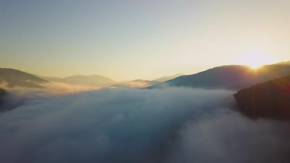 Aerial view of vibrant sunset over white dense foggy clouds with distant dark silhouettes