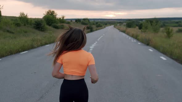 Rear View of Young Girl with Long Hair Jogging on Road at Nature at Sunset
