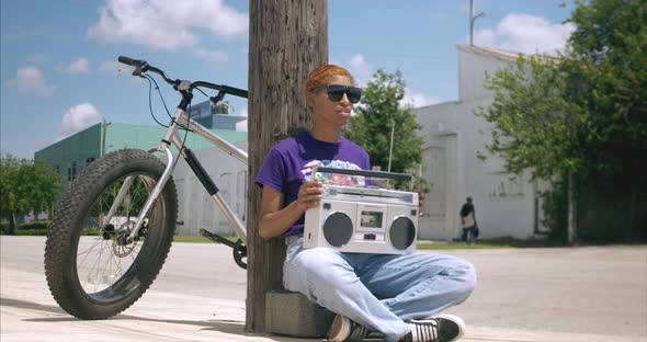 Panning shot of African American female holding boom box while sitting on ground