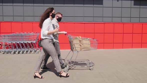 Man and Woman in Face Masks Walking Outdoors after Buying Groceries