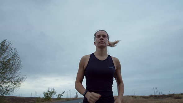 Woman is Jogging Outdoors Concentrating Look in Front of Her Background Cloudy Sky Front View