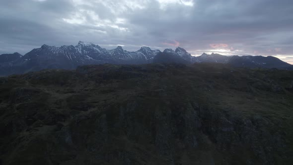 Aerial view over a mountain revealing the dramatic sunset above a snowy range - rising, drone shot