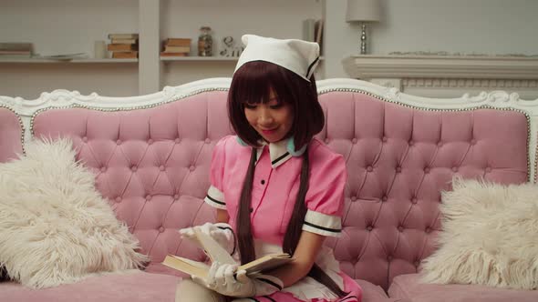 Lovely Asian Woman in Maid Cosplay Costume Reading a Book on Couch