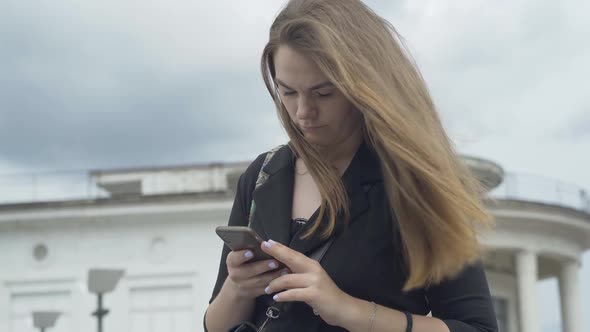 Concentrated Caucasian Woman Typing Message on Smartphone Outdoors. Portrait of Young Beautiful