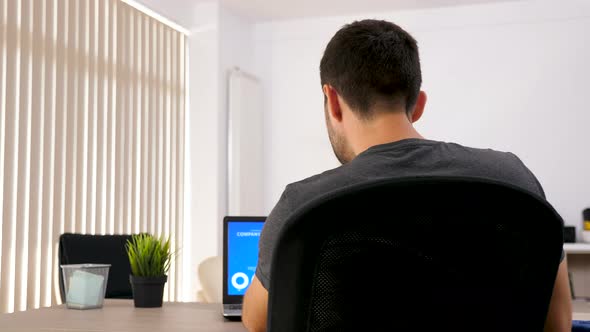 Rear View of Man in His Living Room Looking at Computer Screen with Animated Financial Charts