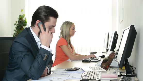 Man Phone and Woman Works on Desktop Computer in the Office (Workers)