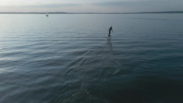 Man Riding on a Hydrofoil Surfboard on Large Blue Lake in Sunny Weather