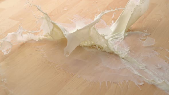 Dropping glass of milk and breaking on wooden floor, Slow Motion