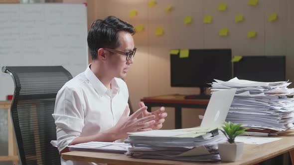 Asian Man Having Video Call On Laptop While Working With Documents At The Office