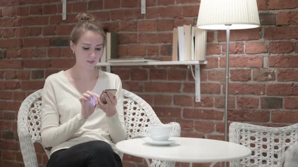 Young Woman Having Coffee and Reacting To Failure on Smartphone