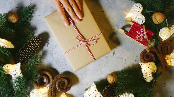 On the Table Against the Backdrop of Festive Toys and Decorations, Female Hands Put a Christmas