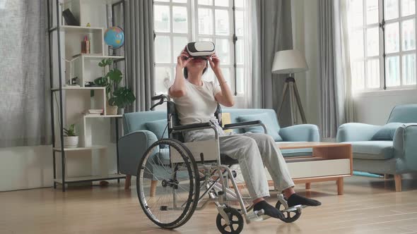 Asian Woman Sitting In A Wheelchair While Wearing Virtual Reality Goggles At Home